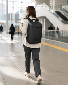 Pendlerin mit schwarzem Horizon Business-Rucksack in Bewegung in einem modernen Bahnhof.
