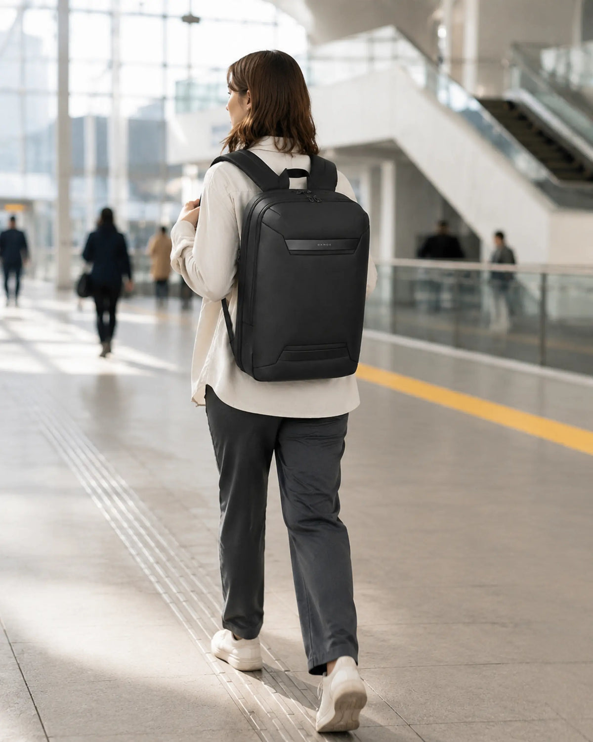 Pendlerin mit schwarzem Horizon Business-Rucksack in Bewegung in einem modernen Bahnhof.