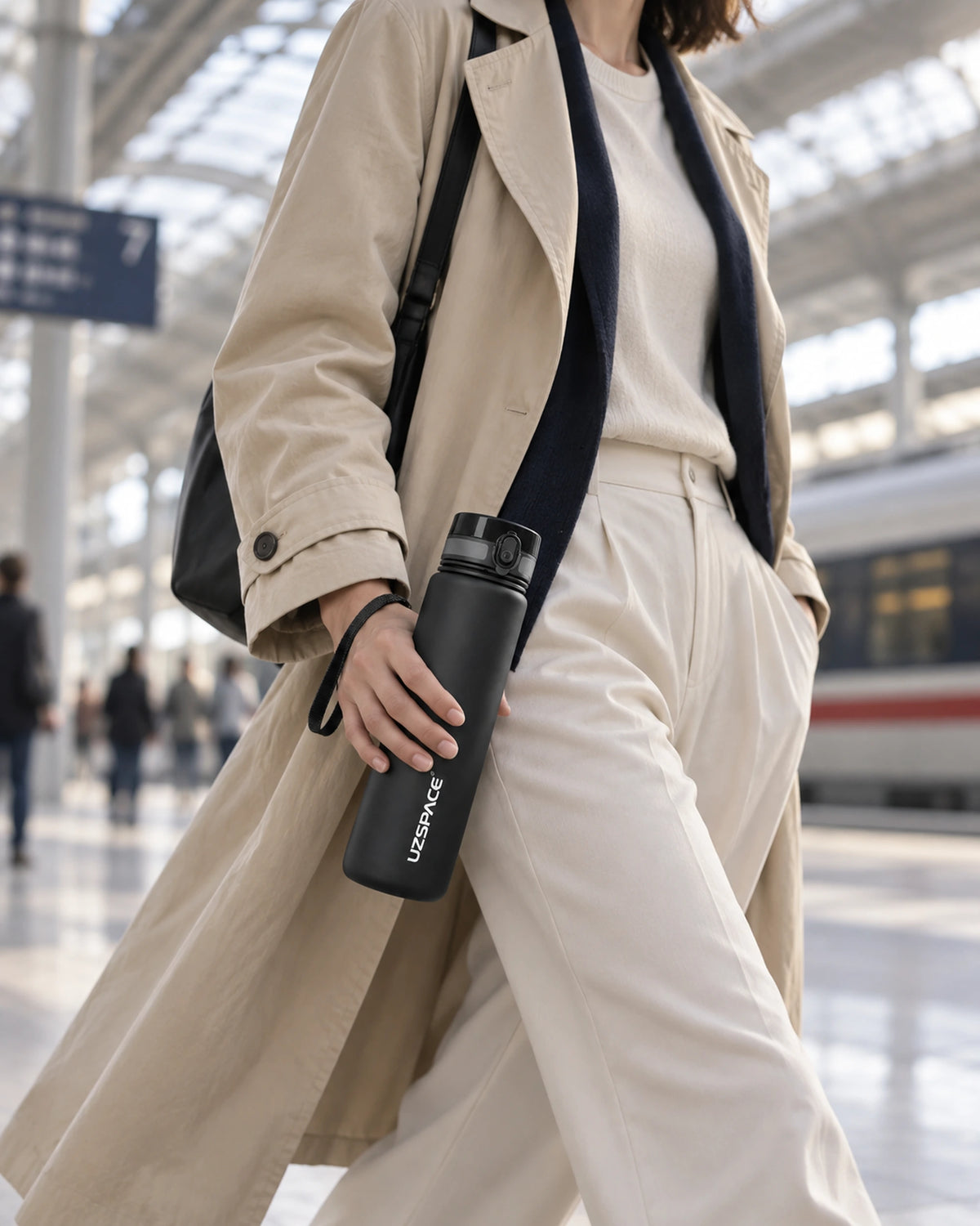 Frau trägt die schwarze CARRYON X HydraGo Trinkflasche beim Gehen durch einen modernen Bahnhof.