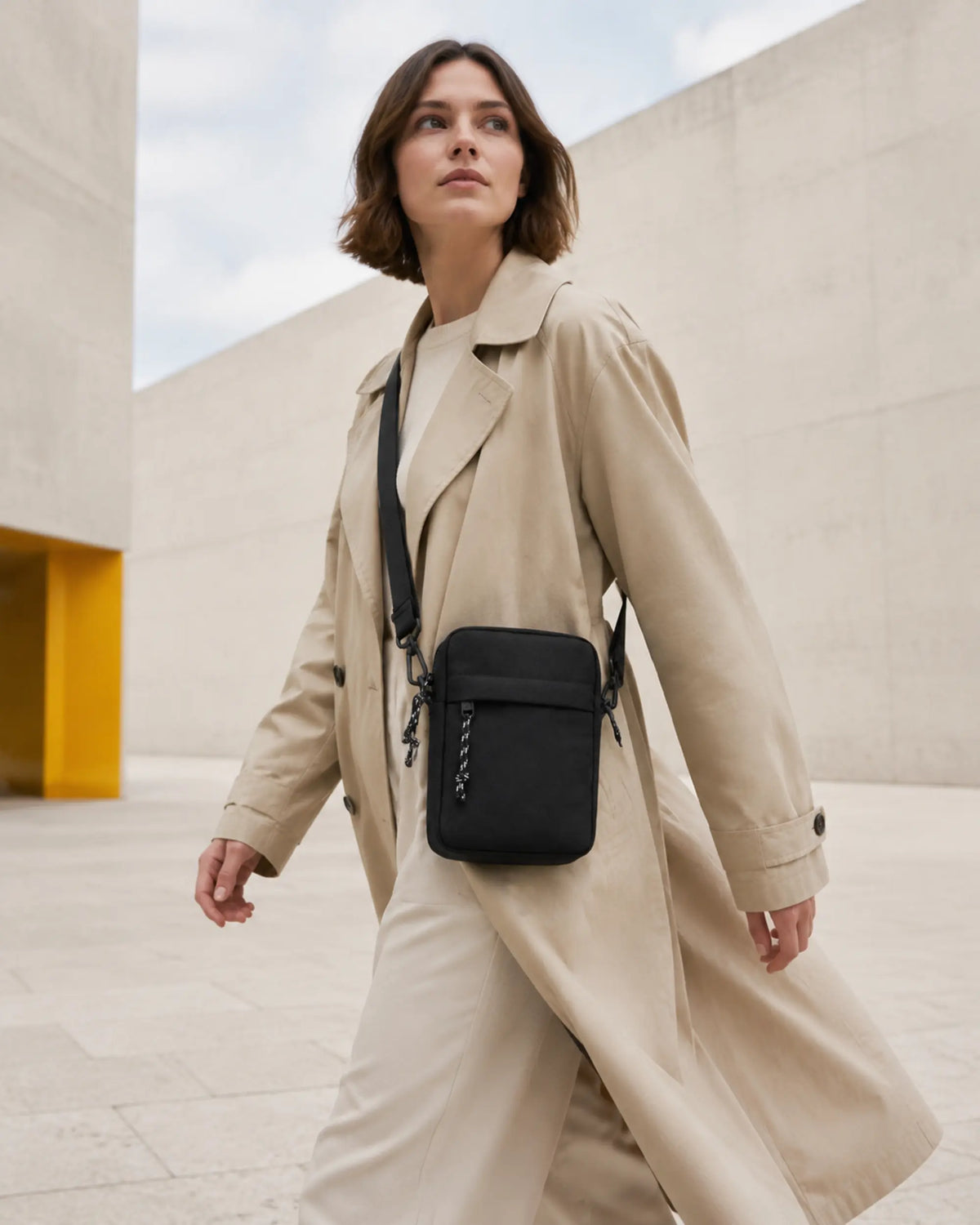 Frau trägt die schwarze UrbanEase Crossbody-Tasche beim Gehen durch einen modernen Museumshof.