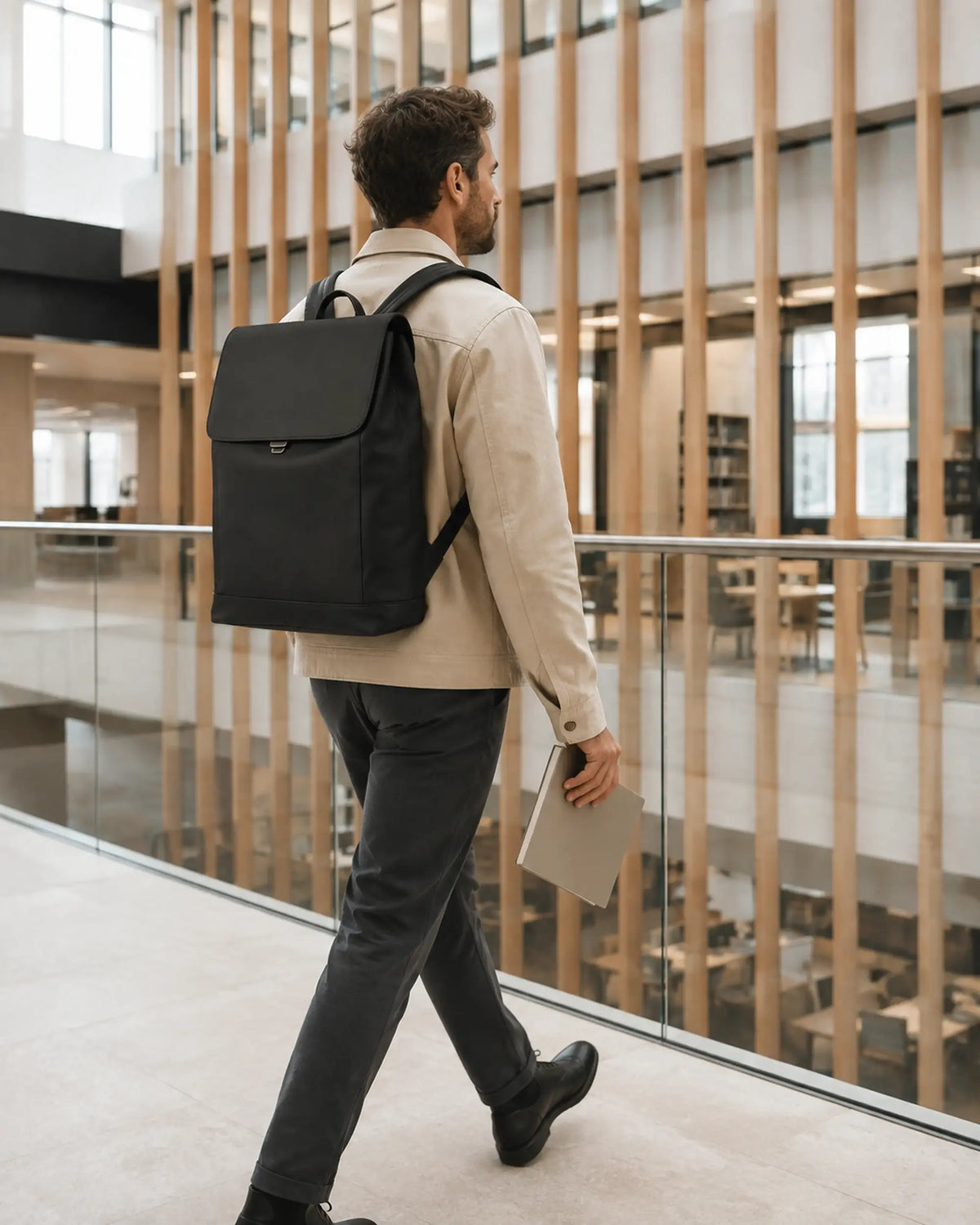 Person mit schwarzem UrbanEdge Rucksack in Bewegung auf einer modernen Campus-Brücke.